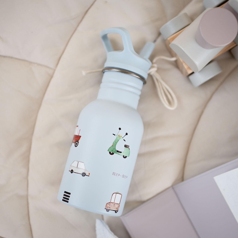May include: A light blue water bottle with a matching blue lid and straw. The bottle is decorated with small illustrations of vehicles, including a scooter and a car. The text "BEEP-BEEP" is printed on the bottle. A white string is attached to the bottle.