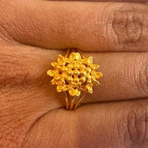 May include: A gold ring featuring a flower design. The flower is crafted from small, round beads and has a textured finish.