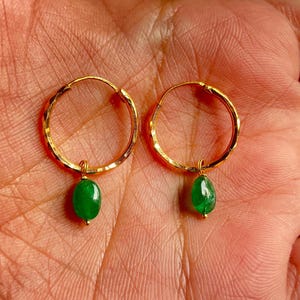May include: A pair of gold hoop earrings with a green gemstone dangling from each hoop.