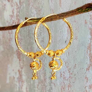 May include: A pair of gold hoop earrings with a textured design. Each earring has a dangling ball charm with a faceted surface.