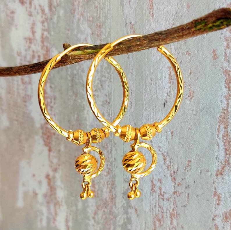 May include: A pair of gold hoop earrings with a textured design. Each earring has a dangling ball charm with a faceted surface.