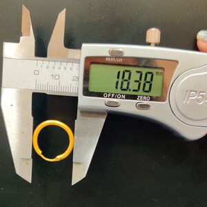 May include: A silver digital caliper measuring a gold ring with a diameter of 18.38 millimeters.
