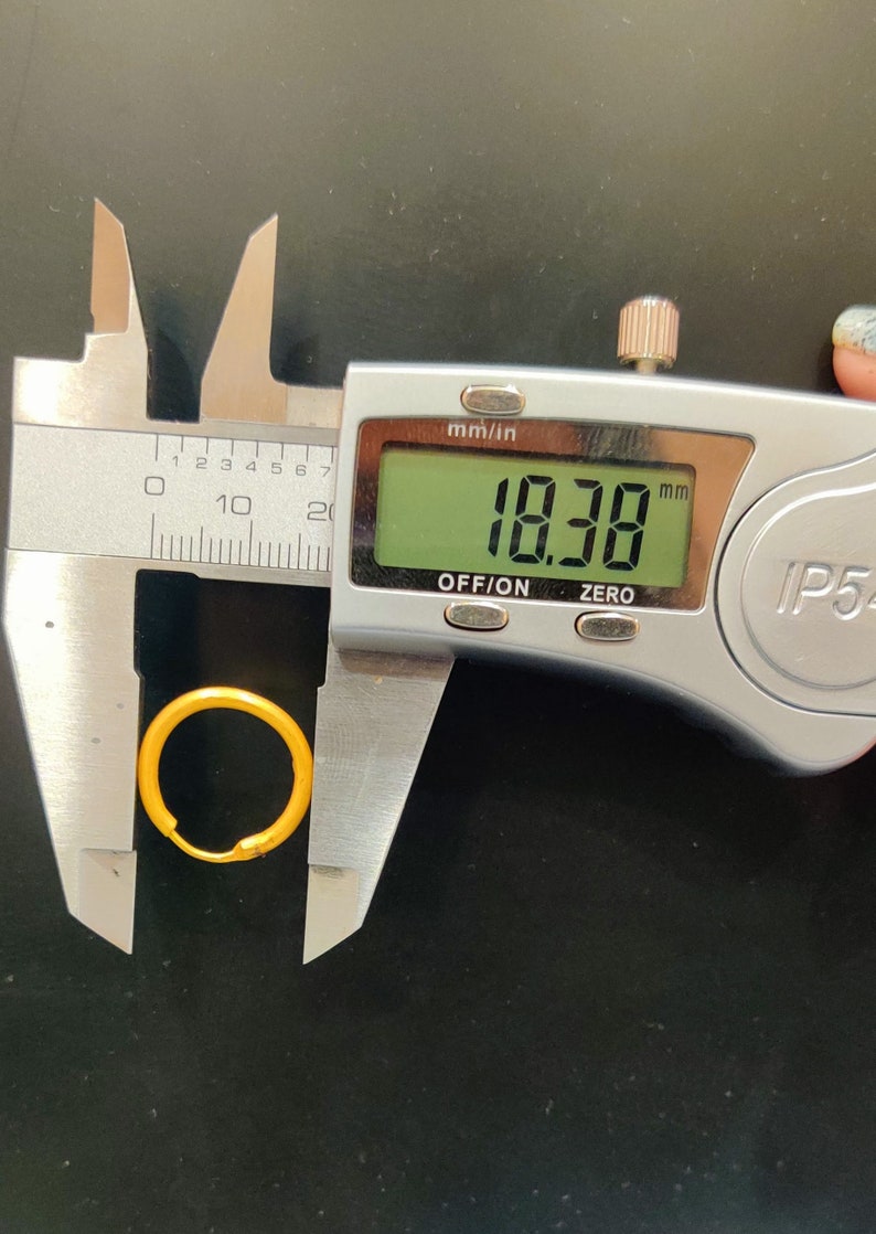 May include: A silver digital caliper measuring a gold ring with a diameter of 18.38 millimeters.