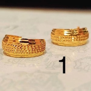 May include: A pair of gold-colored hoop earrings with a textured design. The earrings are made of metal and have a shiny finish.