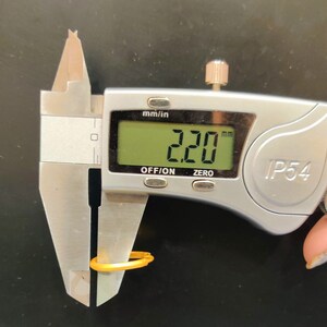 May include: A silver digital caliper measuring a yellow ring. The caliper reads 2.20 mm.