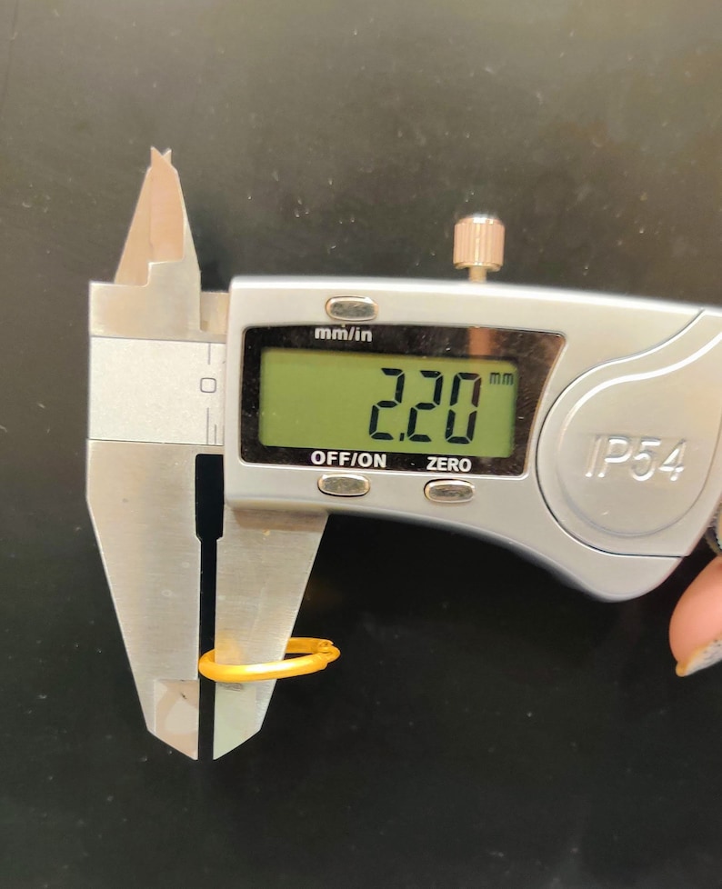 May include: A silver digital caliper measuring a yellow ring. The caliper reads 2.20 mm.