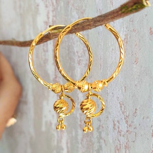 May include: A pair of gold hoop earrings with a textured ball charm hanging from each hoop.