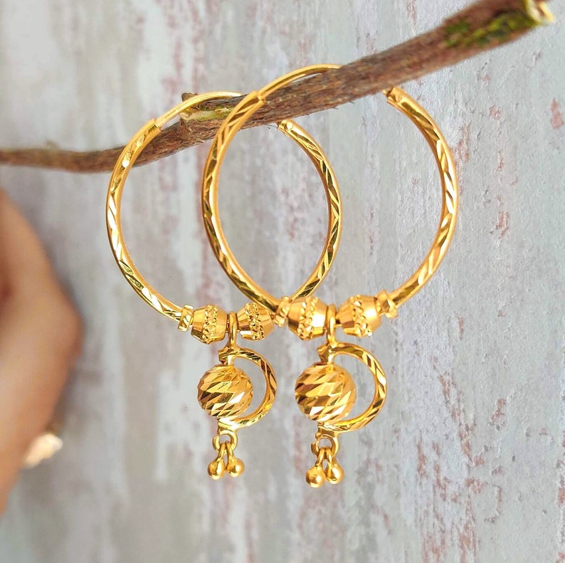 May include: A pair of gold hoop earrings with a textured ball charm hanging from each hoop.