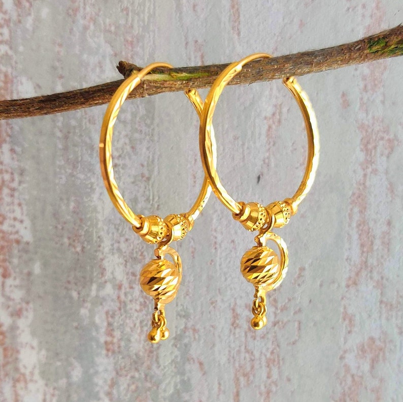 May include: A pair of gold hoop earrings with a textured ball charm hanging from each hoop.