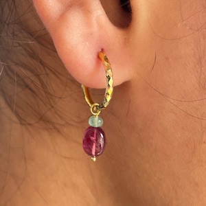 Op de afbeelding: Gouden creolen met een roze en blauwe edelsteen hanger. De creolen zijn getextureerd en hebben een gehamerde afwerking.