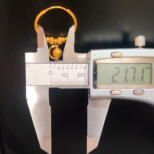 May include: A gold hoop earring with a small, round, decorative charm hanging from it. The earring is measured with a caliper, showing a measurement of 21.71 mm.