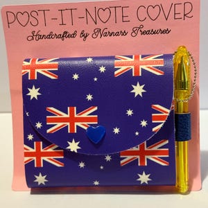 以下が含まれることがあります： オーストラリアの国旗模様、白い星、青いハート型の留め金が付いた青い付箋カバー。青いグリップが付いた金のペンが含まれています。ピンクのカードには「POST-IT-NOTE COVER Handcrafted by Narnars Treasures」と書かれています。
