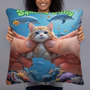 May include: A decorative pillow featuring a cartoon kitten held in hands, with an underwater scene background. The pillow has the text "Squishy Kitty" in green. Dolphins, fish, and coral are visible in the background.