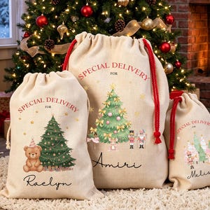 Pode incluir: Três sacos de presente de linho bege com cordões vermelhos. Cada saco apresenta o texto Special Delivery, uma ilustração de árvore de Natal e um nome personalizado. Os sacos exibem gráficos de um urso de peluche, um quebra-nozes e um cavalo de balanço.