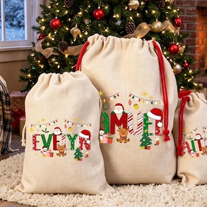 Pode incluir: Três sacos de presente de juta bege com fechos de corda vermelha. Cada saco apresenta uma estampa gráfica festiva com luzes de Natal coloridas, um gorro de Pai Natal, uma pequena árvore de Natal e os nomes Evelyn, Samuel e Kaitlin.