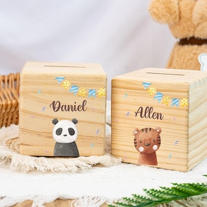 Könnte beinhalten: Zwei hölzerne Sparschweine mit personalisierten Namen, Daniel und Allen. Das Sparschwein mit dem Namen Daniel hat eine Panda-Illustration, während das andere Sparschwein mit dem Namen Allen eine Tiger-Illustration hat. Beide Sparschweine haben ein blaues und gelbes Girlanden-Design.