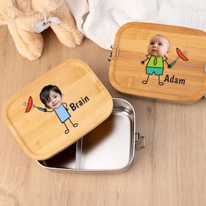 Könnte beinhalten: Zwei personalisierte Bambus-Lunchboxen mit Edelstahl-Innenräumen. Ein Deckel zeigt ein Cartoon-Bild eines Kindes, das einen Hotdog hält, mit dem Namen "Brain". Der andere Deckel hat ein ähnliches Design mit dem Namen "Adam".