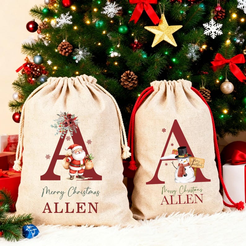 Puede incluir: Dos bolsas de regalo beige con cord&oacute;n de tela. Cada bolsa presenta una letra A granate grande, el texto Merry Christmas y el nombre ALLEN. Una bolsa muestra un gr&aacute;fico de Santa Claus, mientras que la otra muestra un mu&ntilde;eco de nieve con sombrero.