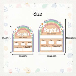 K&ouml;nnte beinhalten: Zwei Holzschilder f&uuml;r den ersten Schultag mit dem Namen "Sophia" und dem Text "First Day Of". Die Schilder sind oben mit einem Regenbogen- und G&auml;nsebl&uuml;mchen-Design gew&ouml;lbt. Das gr&ouml;&szlig;ere Schild ist 28 cm hoch und 22,5 cm breit.