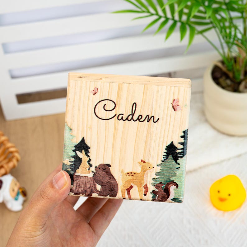 May include: A wooden box with a forest scene and the name "Caden" engraved on the front. The box features a deer, a bear, a rabbit, and a squirrel.
