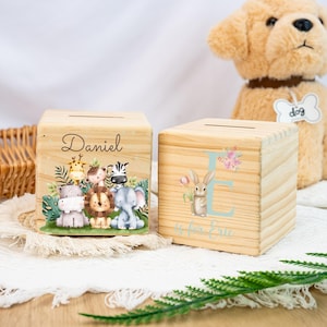 May include: Two wooden money boxes, one with a jungle animal design and the name "Daniel" and the other with a floral design and the letter "E" with the text "E is for Eric".