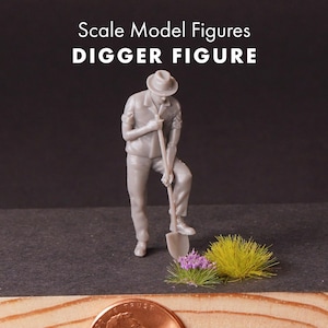 May include: A gray scale model figure of a person wearing a hat and shirt, standing while holding a shovel with one foot on the blade. The text Scale Model Figures DIGGER FIGURE is visible above. A small patch of green and purple grass is nearby.