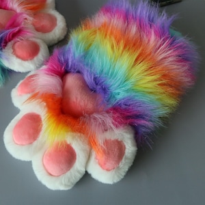 May include: A pair of colorful, furry paw-shaped gloves. The gloves feature a rainbow of colors, including pink, orange, yellow, green, and purple. The paw pads are a soft pink, and the claws are white.