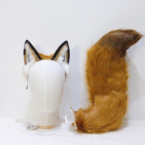 May include: A fox ear headband with black, brown, and white accents, and a matching fluffy orange and brown tail. The ears are attached to a black headband. The tail is large and plush.