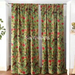 May include: Two green floral curtains with a repeating pattern of red flowers and birds. The curtains are hanging in front of a white wall. The text "KanthaArts" is printed on the curtains.