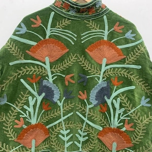 May include: Green velvet jacket with intricate floral embroidery in shades of orange, blue, and teal. The jacket features a high collar and detailed stitching, showcasing a bohemian style.