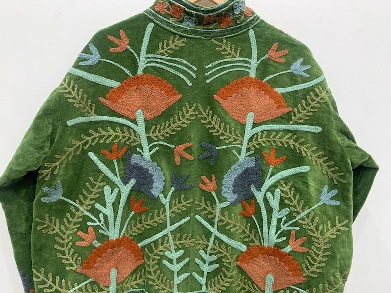 May include: Green velvet jacket with intricate floral embroidery in shades of orange, blue, and teal. The jacket features a high collar and detailed stitching, showcasing a bohemian style.