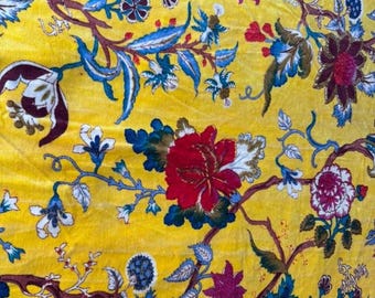 Pode incluir: Close-up de um tecido amarelo com um padrão floral. O design apresenta flores vermelhas, roxas e brancas, juntamente com folhas azuis e caules castanhos. O tecido tem uma textura aveludada.