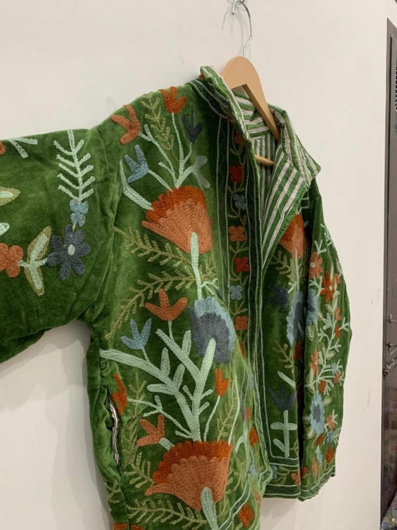 May include: Green velvet jacket with floral embroidery in orange, blue, and white. The jacket features a collared neckline and a striped interior lining. The embroidery includes detailed flower and leaf patterns.