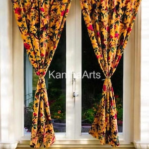 May include: Yellow floral curtains with red flowers and black bird accents hang in front of a window. The curtains are tied back, revealing a glimpse of the outside. The text "Kantha Arts" is visible.