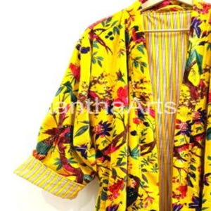 May include: A yellow floral print kimono robe with a vibrant pattern of birds, flowers, and foliage. The robe has a striped lining and rolled-up sleeves with a striped trim. The robe is hanging on a wooden hanger.