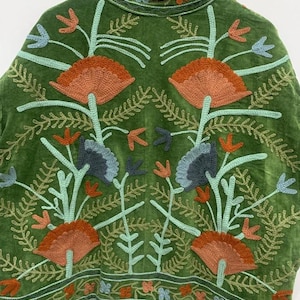 May include: A green velvet jacket with intricate floral embroidery in shades of orange, blue, and green. The jacket features a high collar and a detailed pattern of stylized flowers and leaves, creating a bohemian aesthetic.