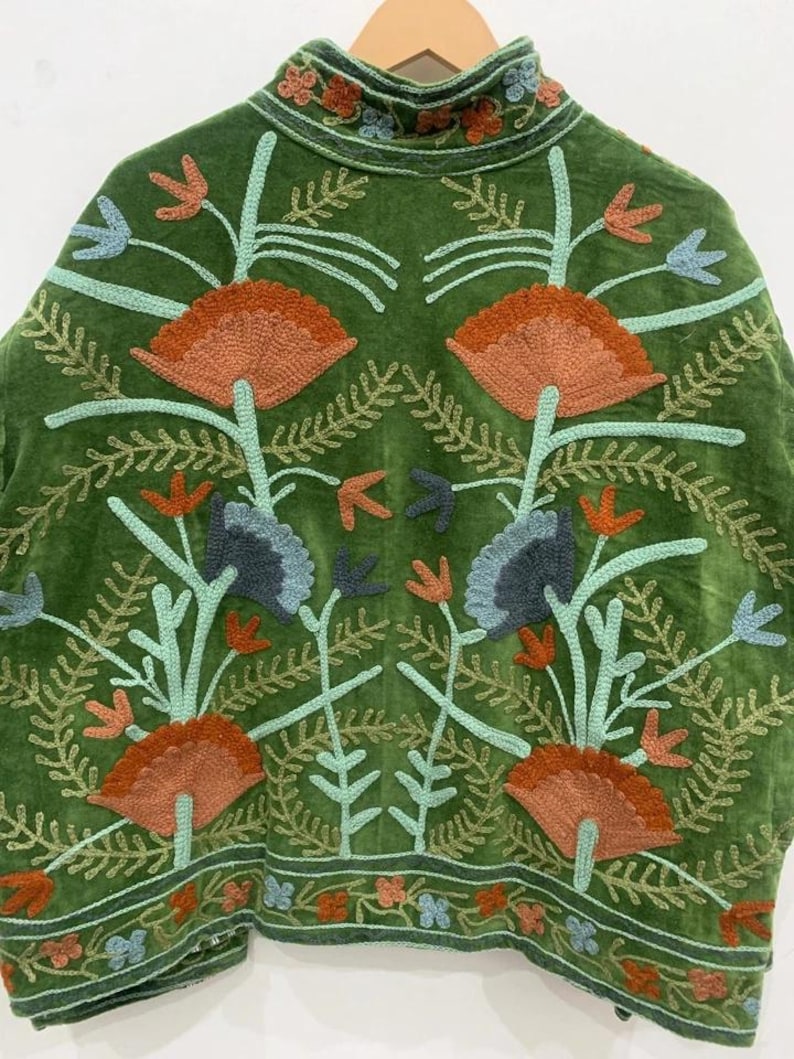 May include: A green velvet jacket with intricate floral embroidery in shades of orange, blue, and green. The jacket features a high collar and a detailed pattern of stylized flowers and leaves, creating a bohemian aesthetic.