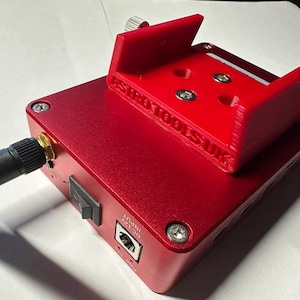 May include: A red metal box with a black antenna and a red plastic phone mount. The box has a power switch, a power input, and the text "ASTRO TOOLS UK" printed on the side.