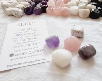 Puede incluir: Un conjunto de piedras pulidas para dormir, que incluyen howlite, amatista, cuarzo rosa, piedra lunar y cuarzo ahumado. Cada piedra está etiquetada con su nombre y propiedades.
