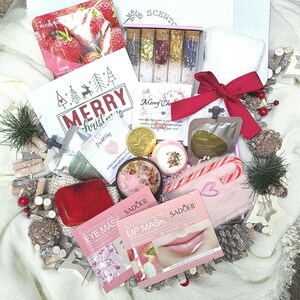 May include: A festive gift box containing beauty products like face masks, bath bombs, and a red bow. The box includes a strawberry face mask, a candy cane, and a small white towel. The text "MERRY Christmas" is visible.
