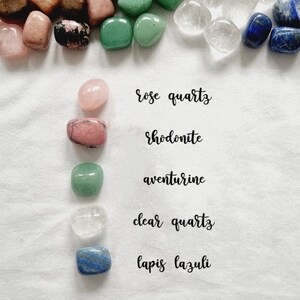 Op de afbeelding: Een verzameling getrommelde stenen, waaronder rozenkwarts, rhodonite, aventurijn, helder kwarts en lapis lazuli. Elke steen is gelabeld met zijn naam.