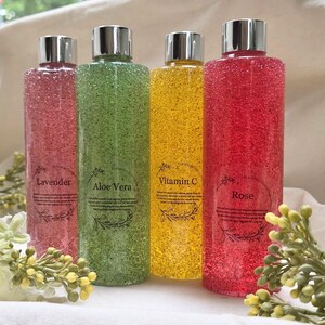 Puede incluir: Cuatro botellas transparentes con tapas plateadas, llenas de l&iacute;quidos de colores. Las etiquetas dicen "Lavanda", "Aloe Vera", "Vitamina C" y "Rosa". Los l&iacute;quidos son rosa, verde, amarillo y rojo. Ilustraciones bot&aacute;nicas.