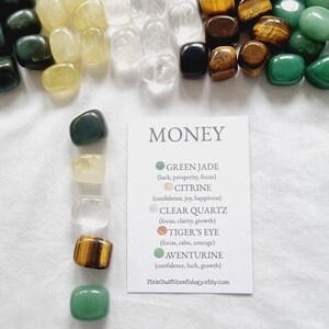 May include: A collection of tumbled stones for prosperity and abundance. The stones are green jade, citrine, clear quartz, tiger's eye, and aventurine. The stones are arranged in a row with a card that lists the stones and their properties. The card reads "MONEY" at the top and lists the stones and their properties below. The card also includes the website address PixieDustScentology.etsy.com.