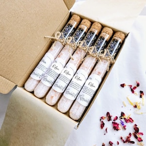 May include: A box containing six glass test tubes filled with bath salts and lavender. The tubes are tied with twine and have cork tops. The label on the tubes reads "Relax".