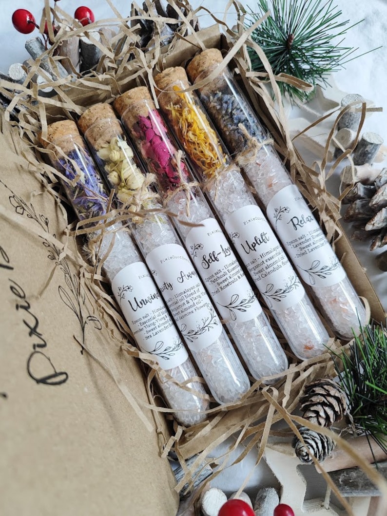 May include: Six glass test tubes filled with dried flowers and bath salts. The tubes are labeled with names like "Unwind" and "Uplift".