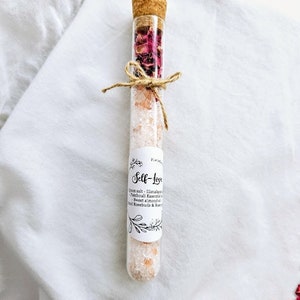 May include: A glass test tube filled with pink Himalayan salt, dried rose petals, and a label that reads "Self-Love" with a list of ingredients: Himalayan salt, Patchouli Essential Oil, Sweet Almond Oil, Rosebuds & Rose Petals.