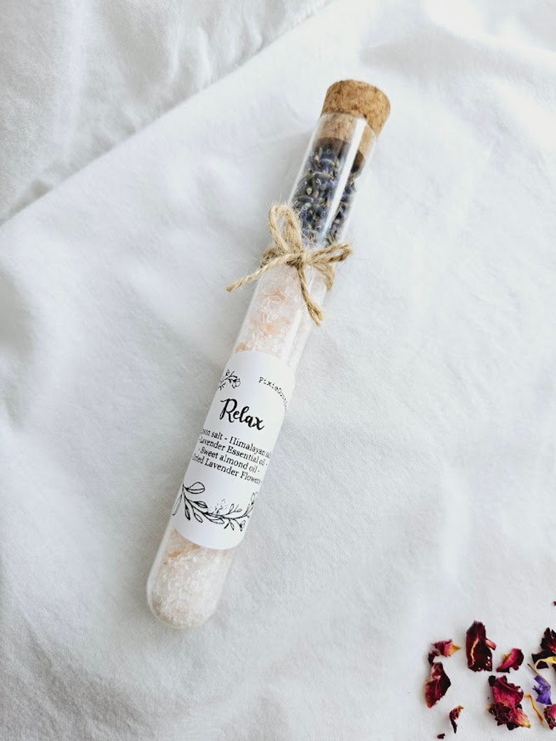 May include: A glass test tube filled with Himalayan salt, lavender essential oil, sweet almond oil, and dried lavender flowers. The label reads "Relax" and lists the ingredients.