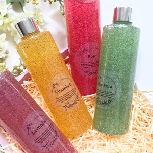 Puede incluir: Cuatro botellas transparentes llenas de l&iacute;quido colorido y texturizado. Las botellas tienen tapas plateadas y etiquetas que dicen "Lavanda", "Vitamina C", "Rosa" y "Aloe Vera". Las botellas est&aacute;n dispuestas en una caja decorativa con paja.