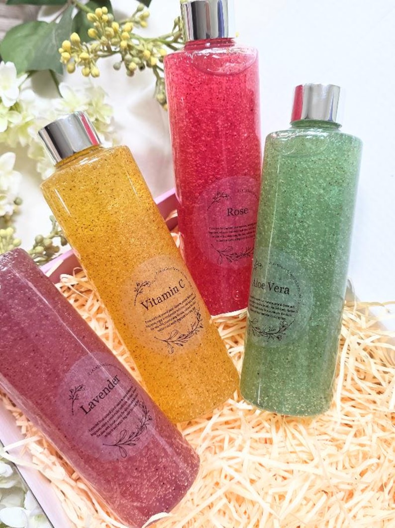 Puede incluir: Cuatro botellas transparentes llenas de l&iacute;quido colorido y texturizado. Las botellas tienen tapas plateadas y etiquetas que dicen "Lavanda", "Vitamina C", "Rosa" y "Aloe Vera". Las botellas est&aacute;n dispuestas en una caja decorativa con paja.