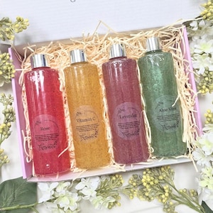 Puede incluir: Un juego de regalo con cuatro botellas transparentes llenas de líquido de colores y tapas plateadas. Las botellas están etiquetadas como "Rose", "Vitamin C", "Lavender" y "Aloe Vera". Presentado en una caja rosa con paja y adornos florales.